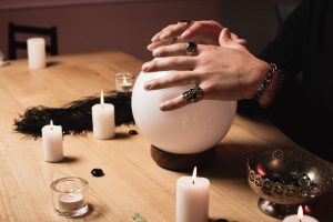 cropped view of psychic holding hands above magical crystal ball near candles